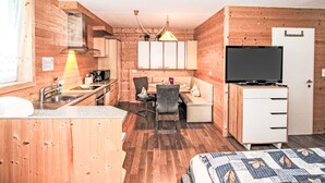 Habitació petita amb parets de fusta, cuineta, zona de menjador, llit i televisió.