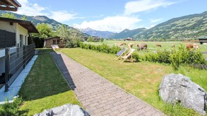 Una propietat rural amb un camí pavimentat, una cabana de fusta i vaques pastant en un camp.