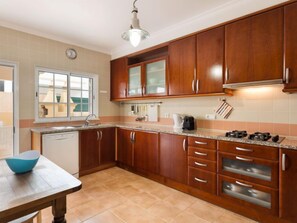 Cocina con alacenas de madera, encimera, lavamanos y ventana.