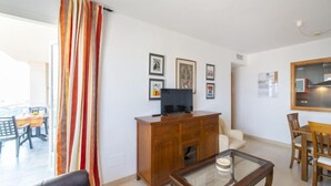 A living room with a wooden cabinet, a glass coffee table, a leather sofa, and a dining area with a table and chairs.