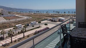 A balcony with a view of a coastal road, palm trees, and a beach.