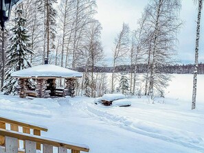 A log cabin with a snow-covered roof, surrounded by a snowy landscape and trees.