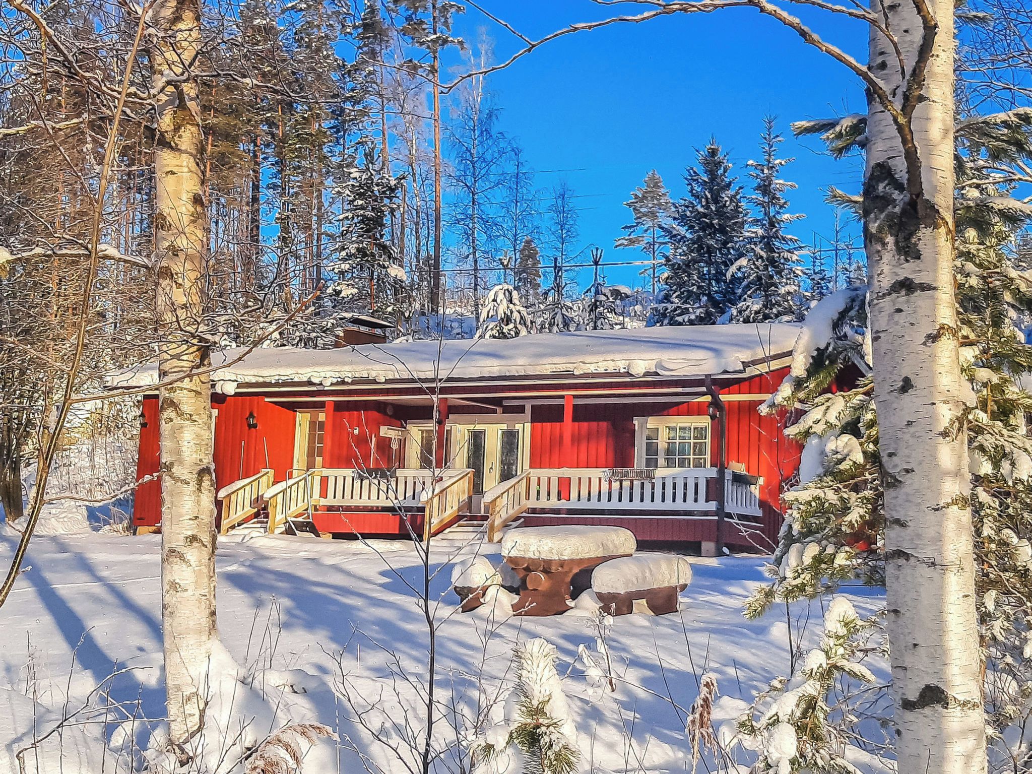 Punainen mökki, jossa on kuisti, ja sen ympärillä on lumipeitteisiä puita.