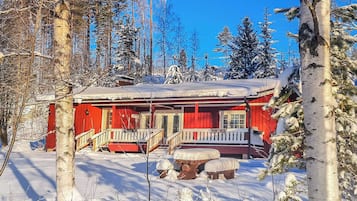Punainen mökki, jossa on kuisti, ja sen ympärillä on lumipeitteisiä puita.