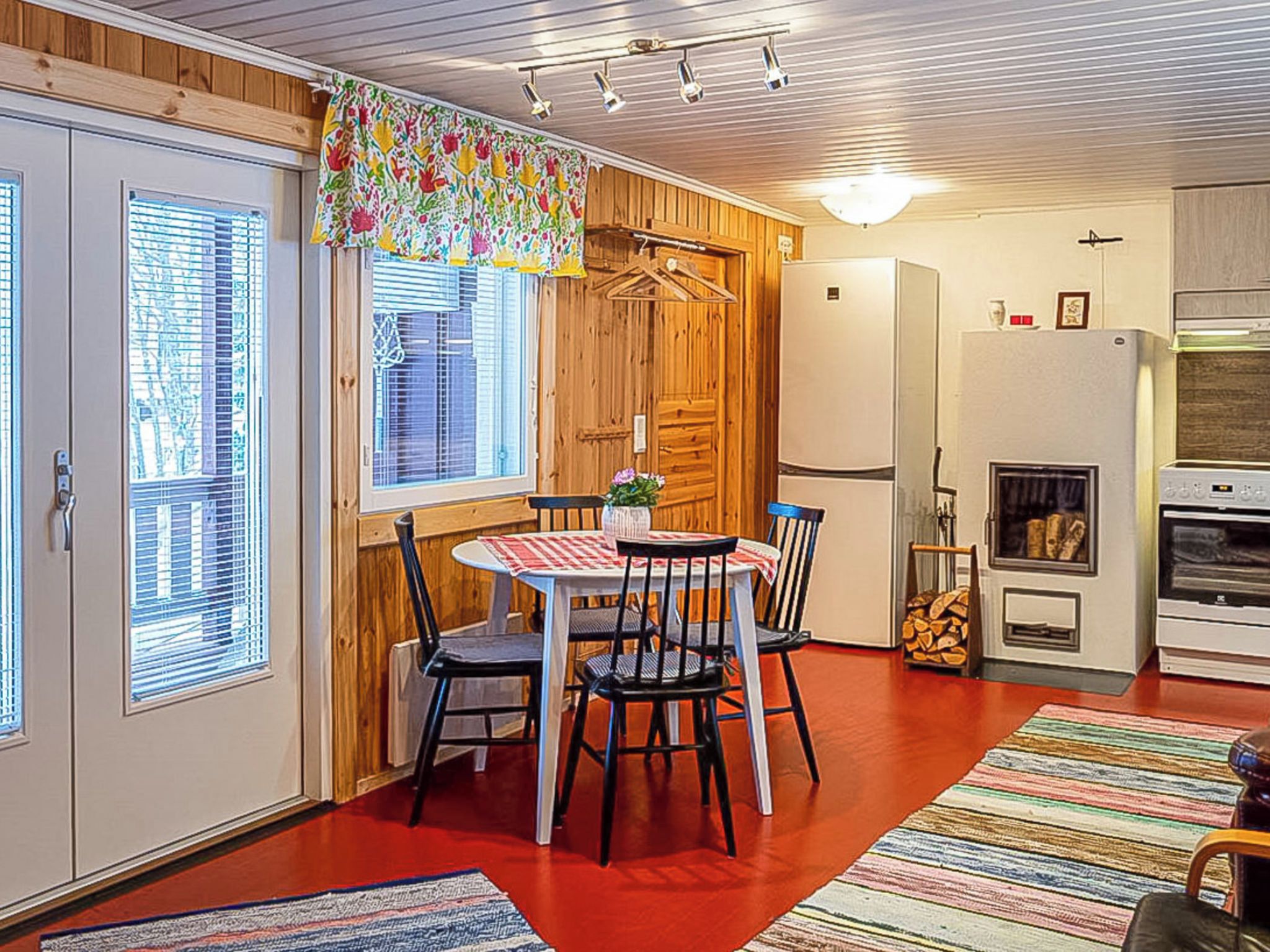 A compact kitchen with a dining area, wooden walls, and a window with blinds.