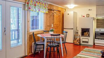 A compact kitchen with a dining area, wooden walls, and a window with blinds.