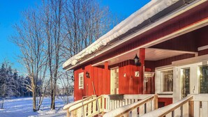 Una baita di legno rossa con un portico in legno e dei gradini che portano a una porta.