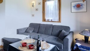 Una sala de estar moderna con un sofá gris, una mesa de comedor dispuesta con vasos y una botella, y una lámpara de techo.