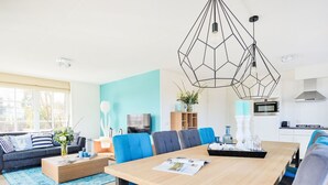 A modern living room with a wooden dining table, blue upholstered chairs, a sofa, and a TV. - Tapuit 6 by Interhome (Noordwijk)