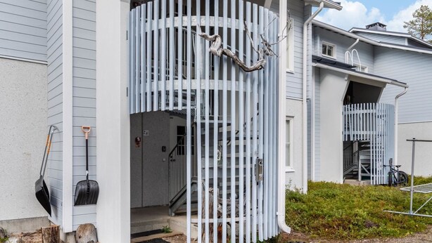Edifício residencial com fachada branca, varanda coberta e escadaria que leva ao segundo andar.