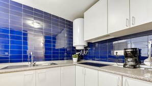 A kitchen with blue tiles, white cabinets, a sink, a coffee maker, and a plant. - Platja de Roses by Interhome (Roses)