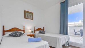 A room with two beds, a small table with a lamp, a picture on the wall, and a view of the outside through a large window. - Platja de Roses by Interhome (Roses)