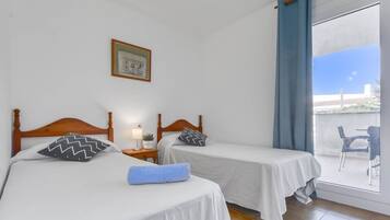 Een kamer met twee bedden, een klein tafeltje met een lamp, een foto aan de muur en uitzicht op buiten door een groot raam.