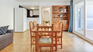 A modern living room with a dining table and chairs, a grey sofa, and a kitchen area with cabinets and a refrigerator. - Platja de Roses by Interhome (Roses)
