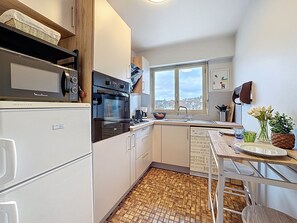 Ett kompakt kök med en inbyggd ugn, mikrovågsugn och ett fönster med utsikt över staden.
