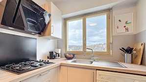 Een keuken met een gasfornuis, een spoelbak, een raam met uitzicht op de stad en een vaatwasser.