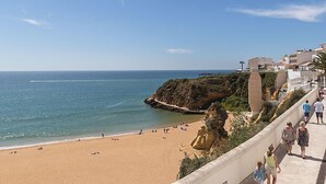 A coastal beach with a rocky outcrop, a sandy beach, and a promenade with people walking. - Dream View 50m from the beach by Interhome (Albufeira)