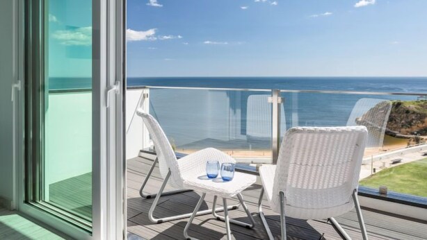 A balcony with a view of the ocean, a table with chairs, and a glass of water. - Dream View 50m from the beach by Interhome (Albufeira)
