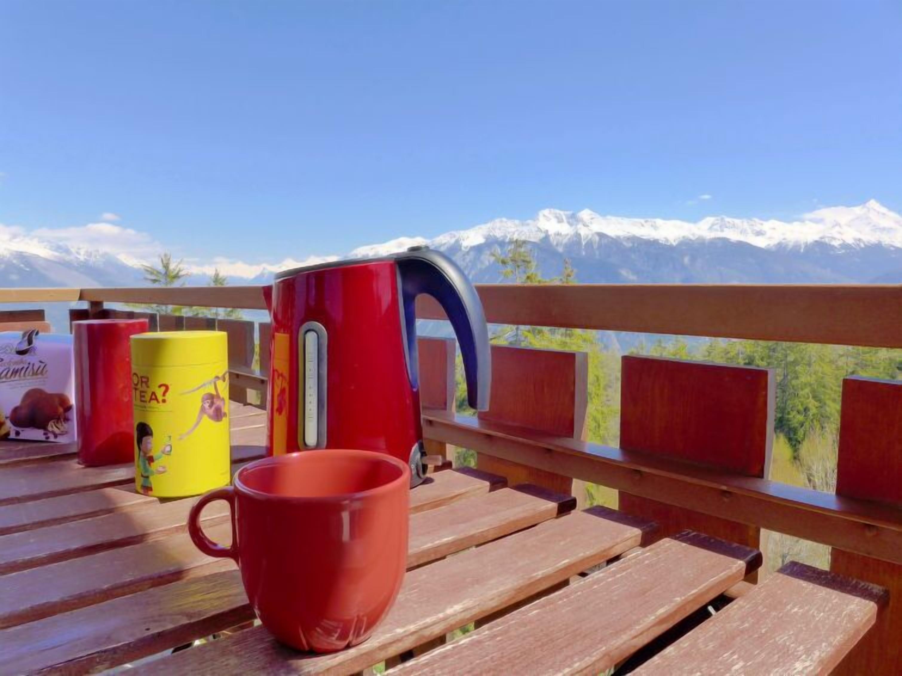 Une terrasse en bois avec une tasse rouge, une tasse jaune et un thermos rouge.