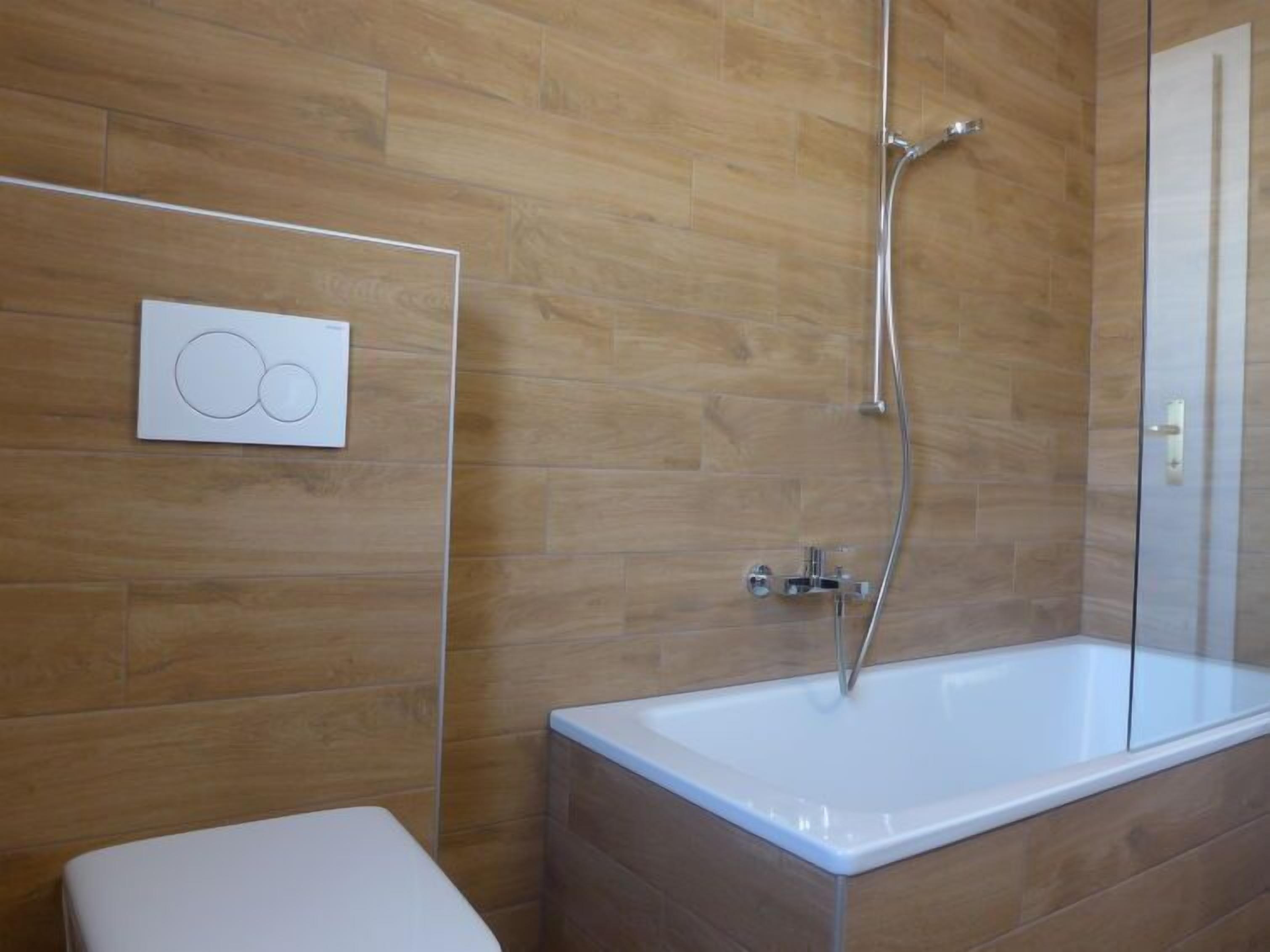 Ein modernes Badezimmer mit Holzboden, einer weißen Badewanne und einer Toilette.