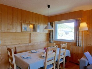 A wooden-paneled room with a dining table set for four, two lamps, and a window with curtains. - Andrea A 10 by Interhome (Crans-Montana)