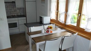 Uma cozinha compacta com armários brancos, micro-ondas e uma mesa de jantar com cadeiras.