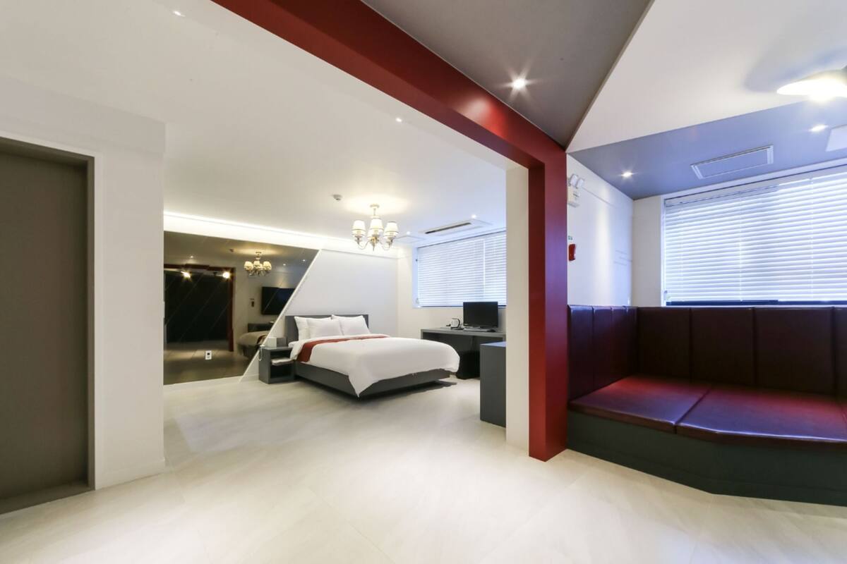 A modern hotel room with a bed, a desk, a TV, and a seating area.