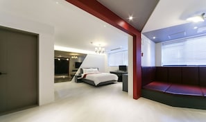 A modern hotel room with a bed, a desk, a TV, and a seating area.