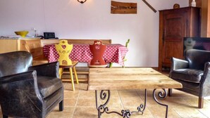 Ein gemütliches Wohnzimmer mit einem Holztisch, zwei Ledersesseln, einem Tisch mit rot-weißer Spitze und einer Holzkabine.