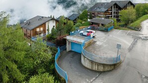 Gebirgslandschaft mit Parkplatz, Gebäuden und einem blauen Zaun.