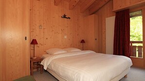 Ein Zimmer mit Holzboden, einem großen Bett, zwei Nachttischen mit Lampen, einem kleinen Stuhl und einem Fenster mit Vorhängen.