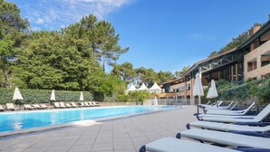 Ein Poolbereich mit Liegestühlen und Sonnenschirmen, umgeben von Bäumen und einem Gebäude im modernen Stil.