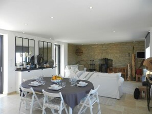A modern living room with a stone wall, a fireplace, and a dining area with a round table and white chairs.