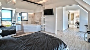 A modern bedroom with a large bed, a bathtub, a TV, and a view of the sea. - Le Ménez by Interhome (Penmarc'h)