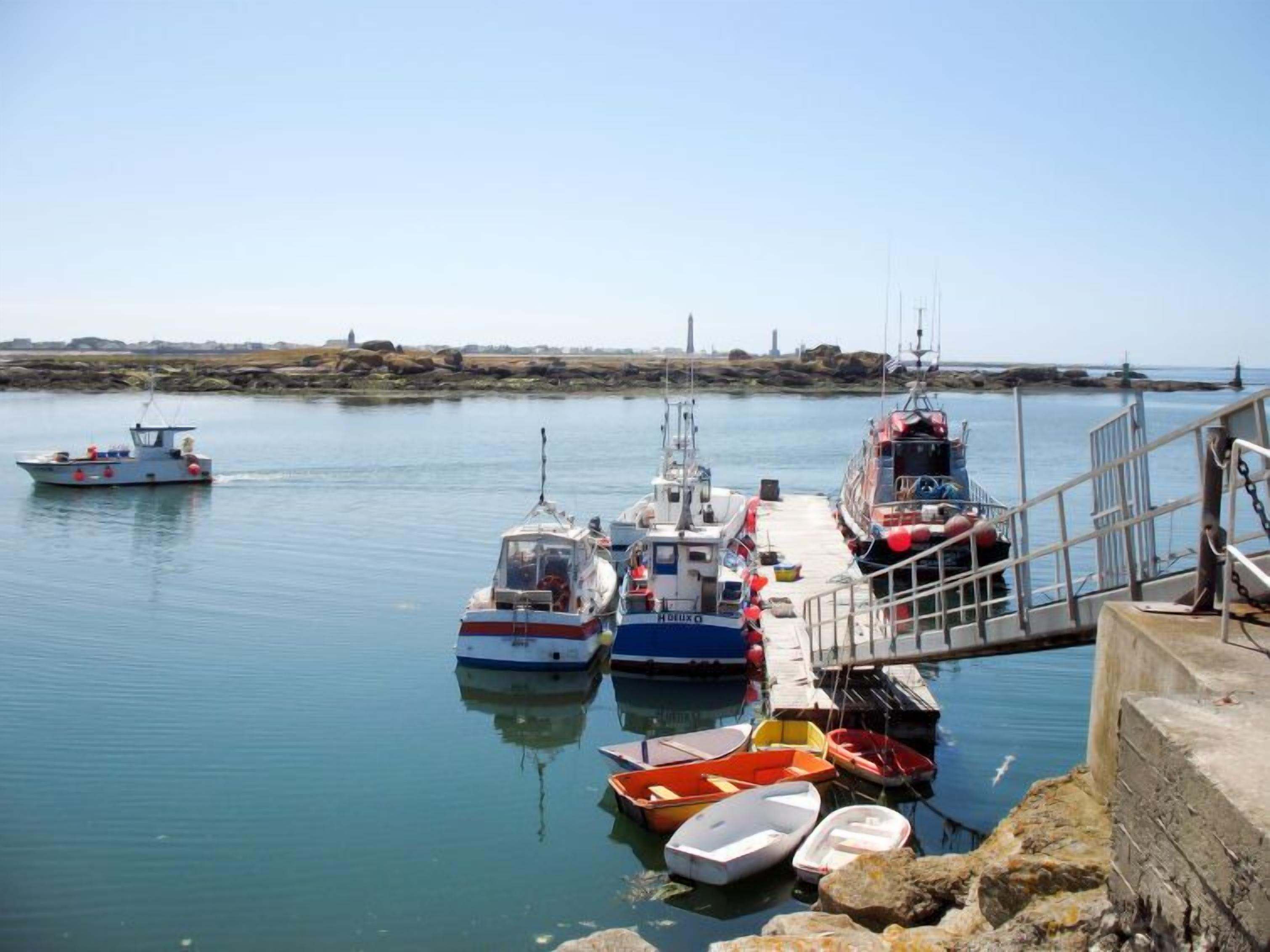 Un puerto con varias embarcaciones amarradas, un muelle y un litoral rocoso.