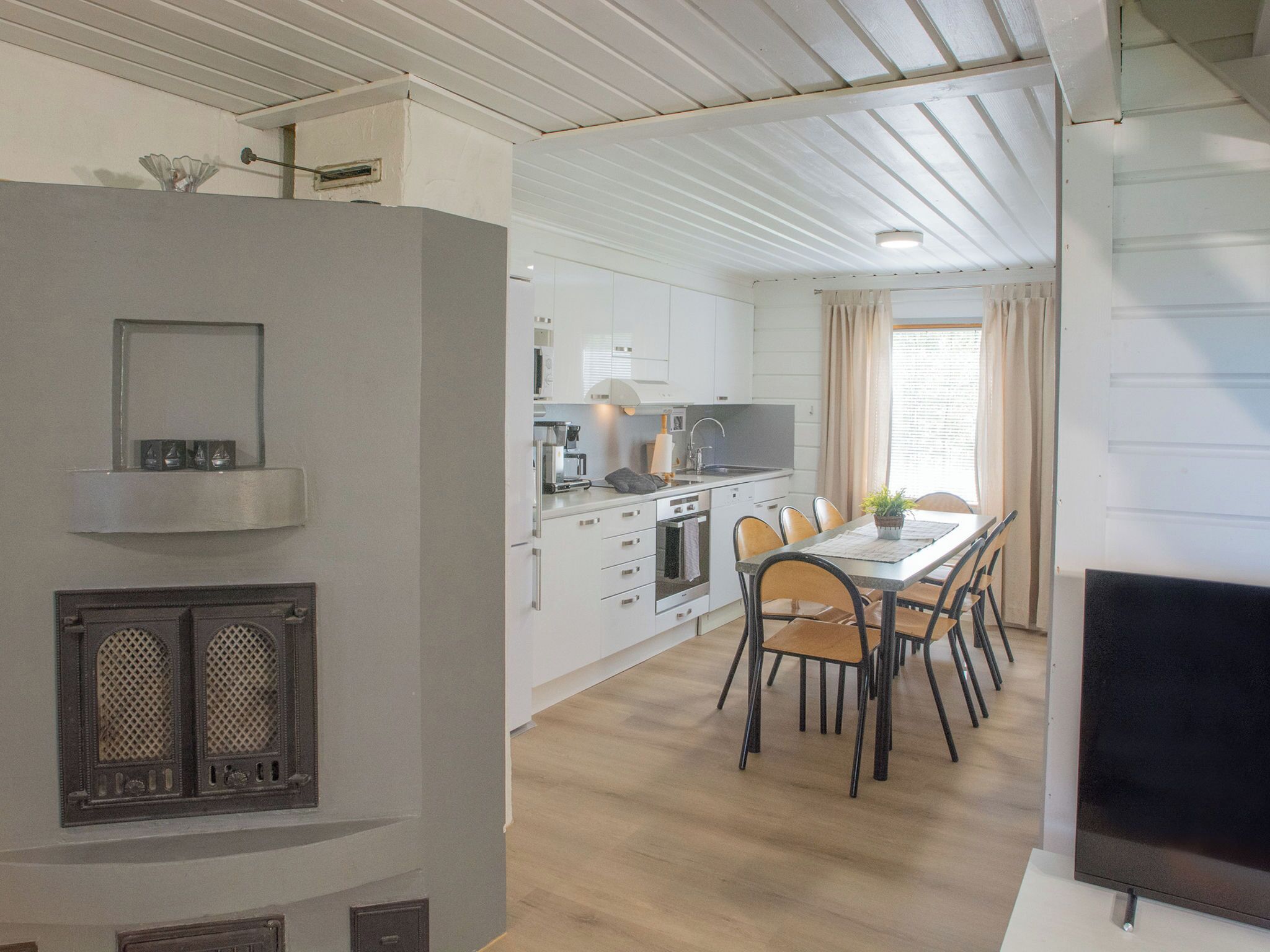 A modern kitchen with white cabinets, a dining area with a table and chairs, and a TV on a stand.