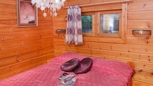 Una habitación de cabaña de madera con cama, lámpara colgante y ventana con cortinas.