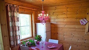 Interior de una cabaña de madera con una mesa para dos, una araña y un refrigerador.