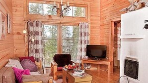 Un acogedor interior de cabaña de madera con sofá, sillón, televisor y chimenea.