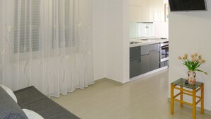 En moderne stue med en sofa, et lille bord med en vase og et køkken i baggrunden.