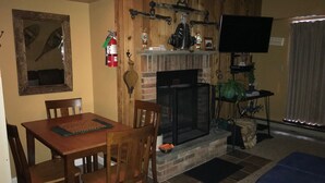 A living room with a fireplace, wooden walls, a television, and a dining area with chairs and a table. - Snowshed & Ramshead Ski Lodges in walking distance plus shuttle service (Killington)