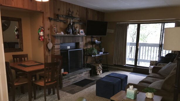 A living room with a fireplace, a television, and a dining area with chairs and a table. - Snowshed & Ramshead Ski Lodges in walking distance plus shuttle service (Killington)