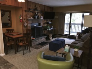 A living room with a fireplace, a television, and a dining area with chairs and a table. - Snowshed & Ramshead Ski Lodges in walking distance plus shuttle service (Killington)