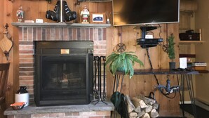 A cozy living room with a fireplace, a flat-screen TV mounted above it, and a rustic wooden wall. - Snowshed & Ramshead Ski Lodges in walking distance plus shuttle service (Killington)