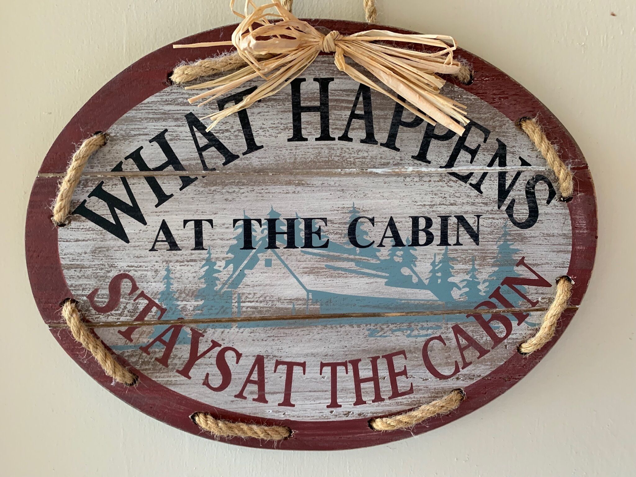 Ein rundes Schild mit dem Text 'What Happens at the Cabin' und 'Stay at the Cabin', umgeben von Seilen.
