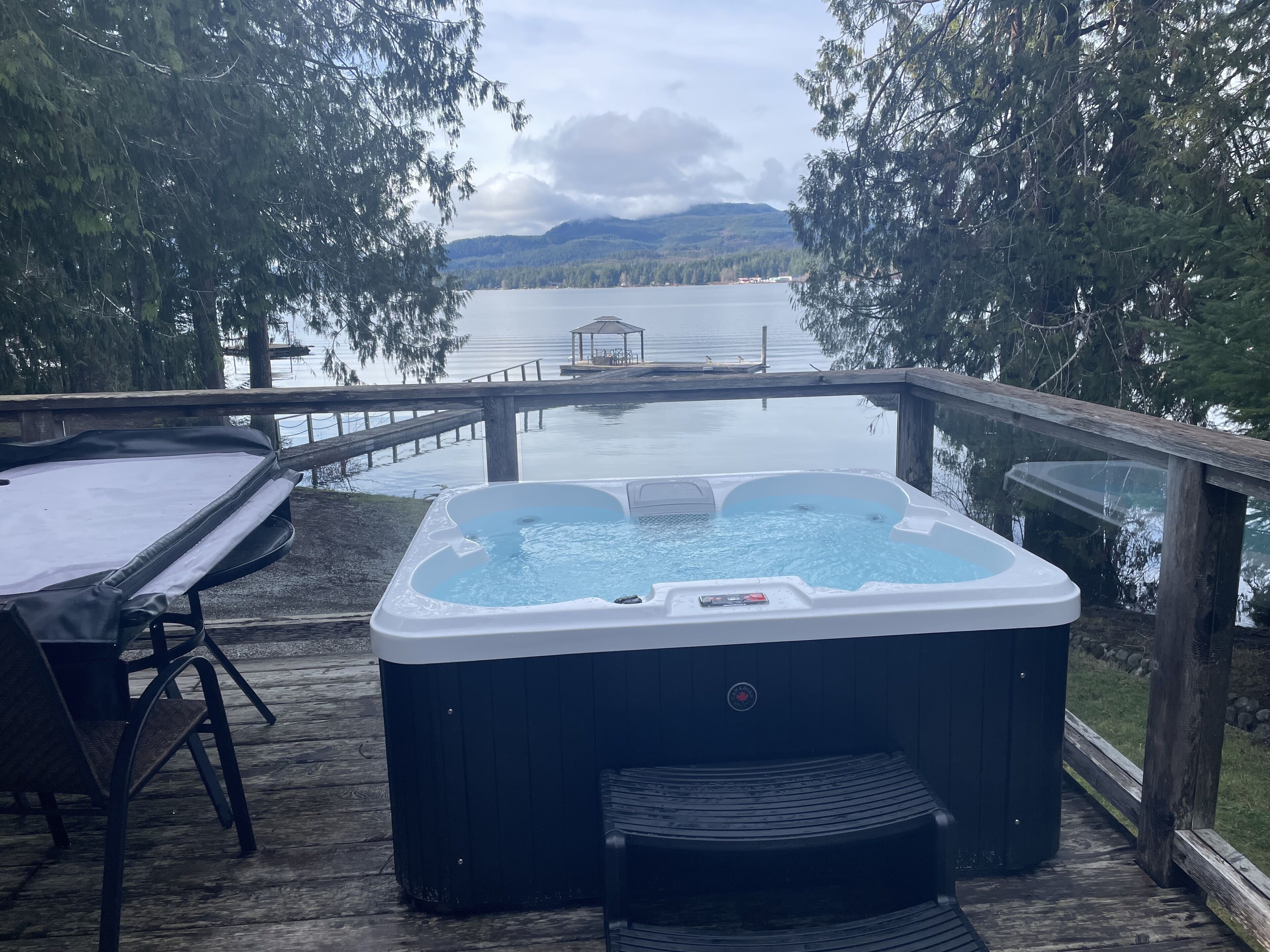 Een hottub op een houten terras, met uitzicht op een meer en bergen.