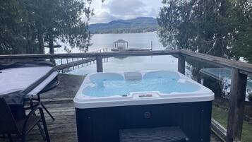 Een hottub op een houten terras, met uitzicht op een meer en bergen.