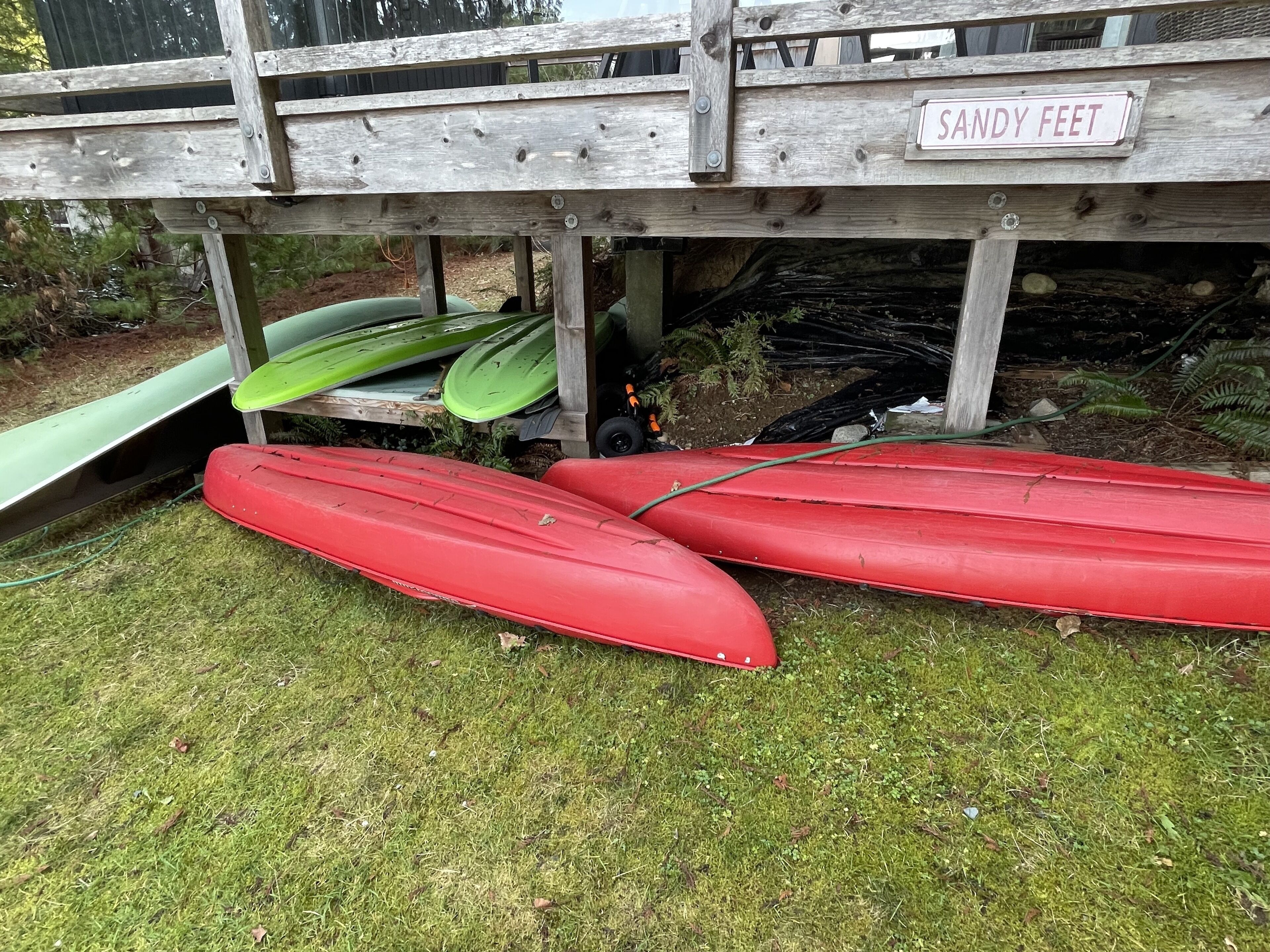 Una struttura in legno con la scritta 'SANDY FEET' e kayak riposti sotto.