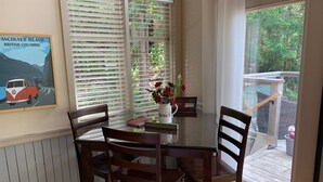 A dining area with a table, chairs, a vase with flowers, a framed picture, and a window with blinds.