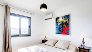 A modern bedroom with a large bed, a window, an air conditioning unit, a colorful abstract painting, and two bedside tables with lamps. - Résidence Cita di Sali by Interhome (Porto Vecchio)